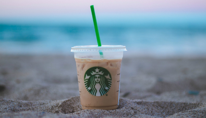 Imagem de um copo da loja Starbucks na areia da praia