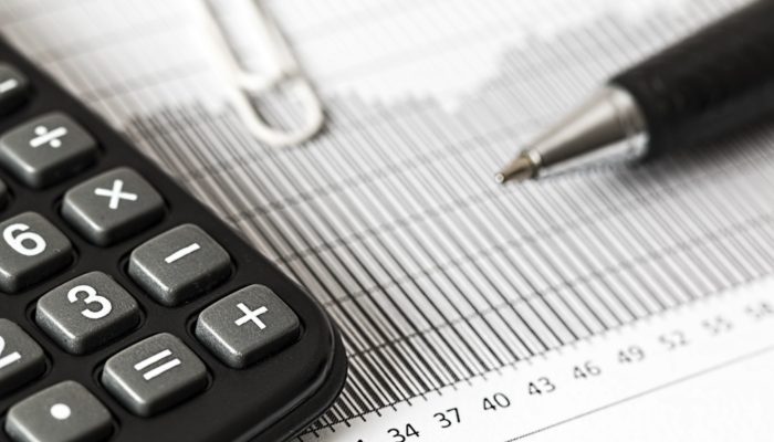 6 dicas para reduzir os custos iniciais do seu negócio Caneta e calculadora sobre planilha impressa, representando como reduzir custos