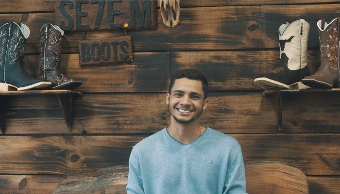 Luis Eduardo Martins, fundador da 7MBoots, sorri em frente a parede de madeira