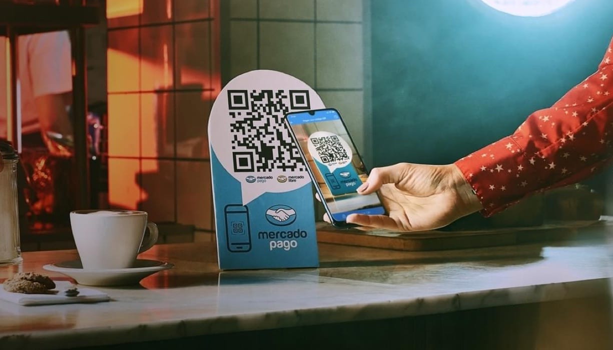 Celular apontando para um QR code em uma plaquinha azul, representando como cobrar pelo Mercado Pago