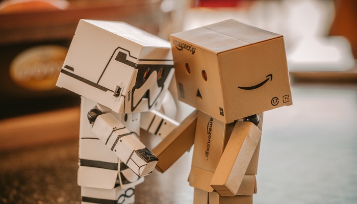 O que é bot e como utilizar essa tecnologia no e-commerce Dois pequenos robôs de papelão, representando a pergunta