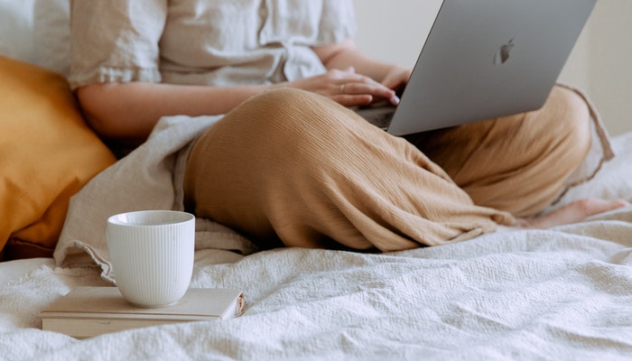 Como começar a vender online com uma loja virtual na pandemia? Mulher na cama, com notebook no colo, representando como vender online durante a pandemia