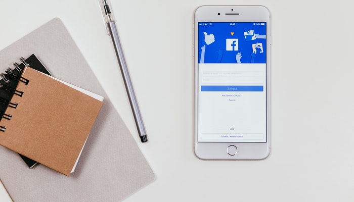 Anotadores, una lapicera y un smartphone que muestra el inicio para hacer publicidad en Facebook.