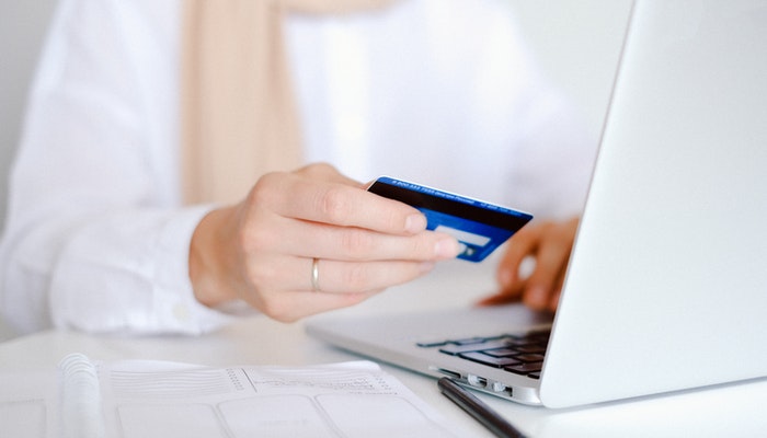O que é o Mercado Pago e como usar em sua loja virtual Imagem de uma mulher segurando um cartão de crédito em frente a um computador. Representando uma compra online.