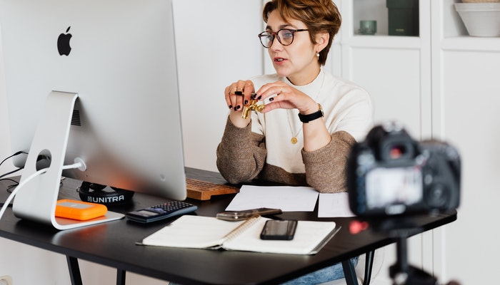 Imagem de uma mulher em seu escritório gravando vídeos para sua empresa, representando a venda de serviços na internet.