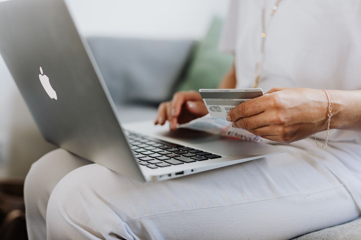 Persona comprando en e-commerce con tarjeta de crédito en la mano y computadora portátil