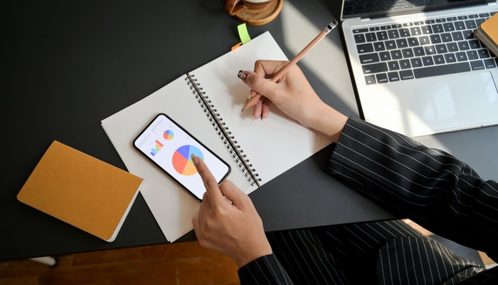 Como aprimorar a experiência do cliente utilizando a análise de dados Imagem mostrando um gráfico e uma pessoa fazendo anotações no caderno, representando a análise de dados para melhorias na experiência do cliente