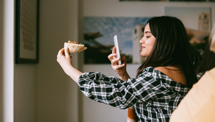 Mulher tirando foto de um pedaço de pizza representando uma postagem no Instagram.