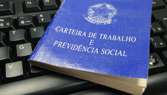 É possível manter uma loja virtual e o emprego ao mesmo tempo? Imagem de uma carteira de trabalho sobre um teclado de computador, representando o emprego e a loja virtual