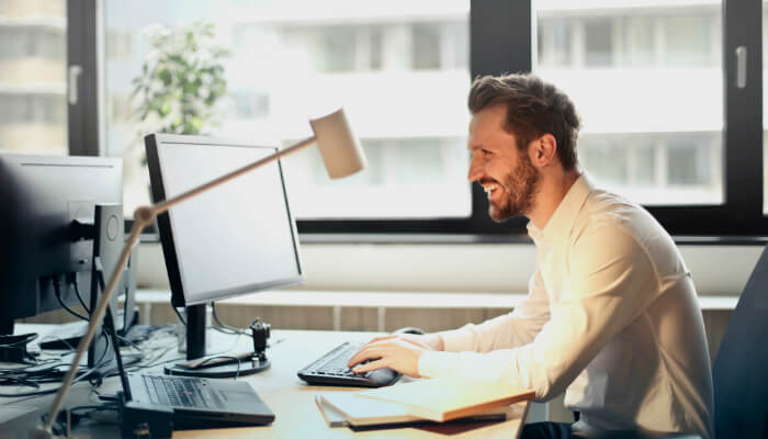 Homem de camisa social sorrindo enquanto mexe no computador, representando estratégias de marketing para LinkedIn
