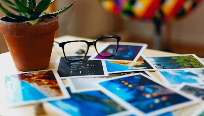 5 dicas de marketing para o Pinterest Mesa com fotos no estilo Polaroid espalhadas em cima, com par de óculos sobre elas, representando o marketing no Pinterest