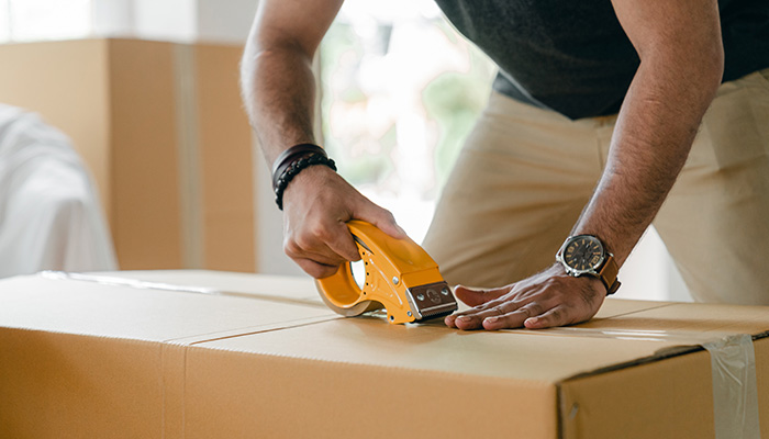Manos de hombre embalando una caja para hacer logística inversa en e-commerce.