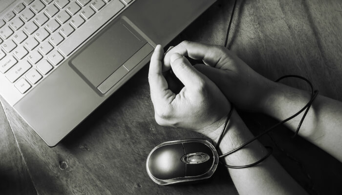 Estatísticas sobre fraude online na América Latina Mãos amarradas com fio de mouse de computador, representando as fraudes virtuais