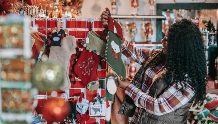 4 truques de design para deixar a sua loja com a cara do Natal Mulher em loja com enfeites natalinos representa do background de Natal