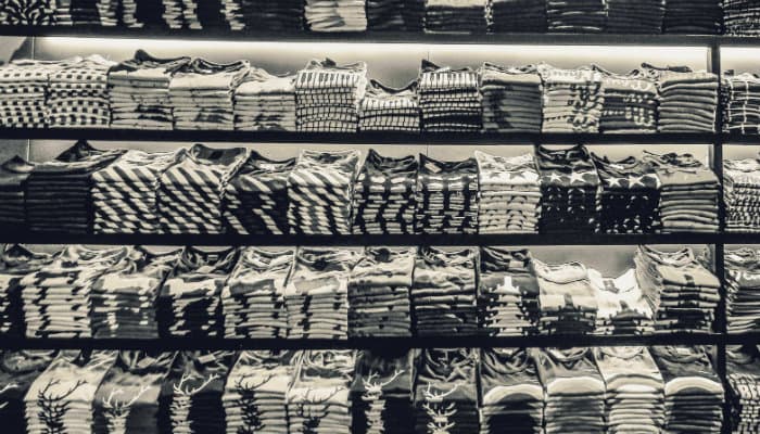 Quando abrir uma confecção de camisetas e como precificar o produto Imagem mostrando diversas pilhas de camisetas em prateleiras.
