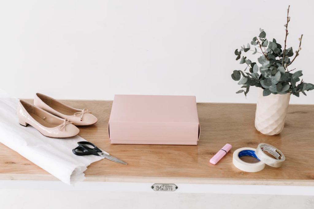 Zapatos de mujer, caja, tijeras, cinta adhesiva y otros materiales de envío sobre una mesa