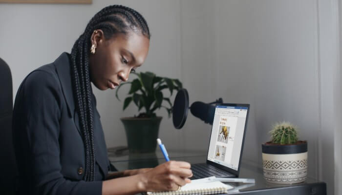 Empreendedora em frente a computador escreve em caderno, anotando instruções de como se cadastrar no MEI