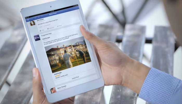 Guia completo de marketing para o Facebook Mãos de homem seguram um tablet aberto no feed do Facebook