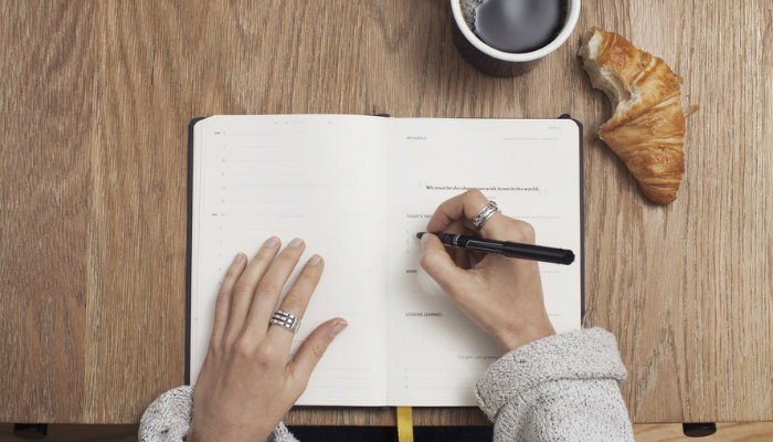 Como e por que cadastrar clientes em sua loja virtual? Pessoa escrevendo em agenda para cadastrar clientes
