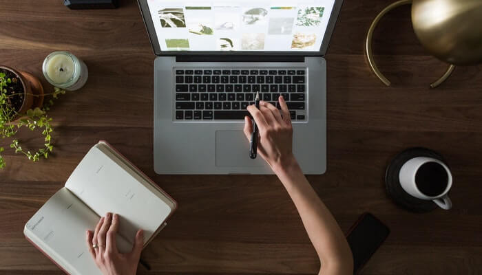 Como cadastrar um domínio próprio na sua loja virtual? Mulher mexe em computador e anota em caderno, representando como cadastrar domínio