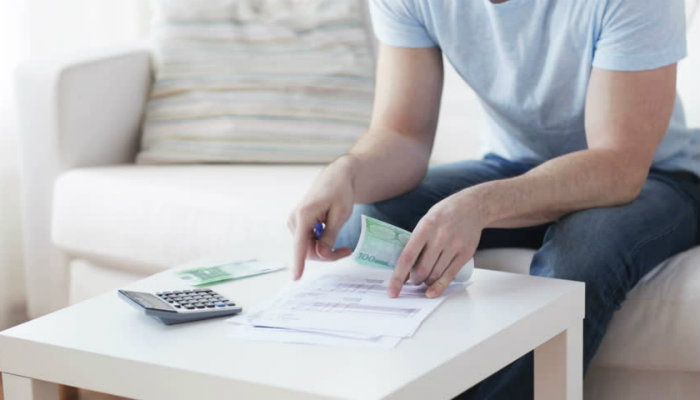 Como tomar boas decisões econômicas em sua loja virtual: o diagnóstico financeiro Homem lê papel, em mesa com cédulas e calculadora, representando o diagnóstico financeiro