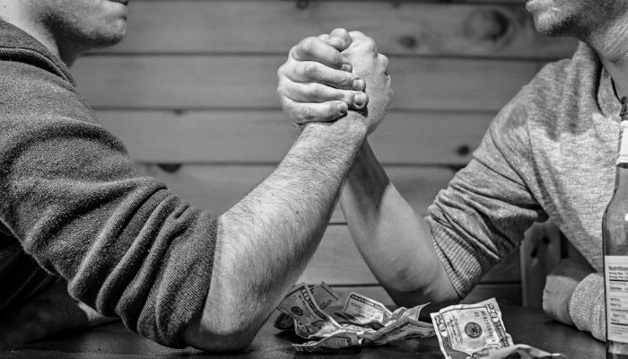 Google Ads X Facebook Ads: qual a melhor escolha para o seu negócio? Homens em disputa de braço de ferro, representando Google Ads versus Facebook Ads