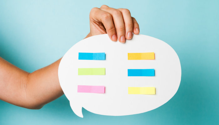 4 dicas fundamentais para criar um conteúdo engajador em sua página no Facebook Mão segura papel em formato de balão de fala com post its coloridos, representando o os conteúdos para Facebook