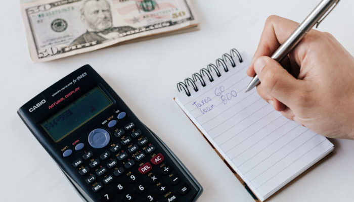 Cómo calcular el precio de un producto (incluye plantilla gratis) Persona haciendo fijación d eprecios con una calculadora y una libreta