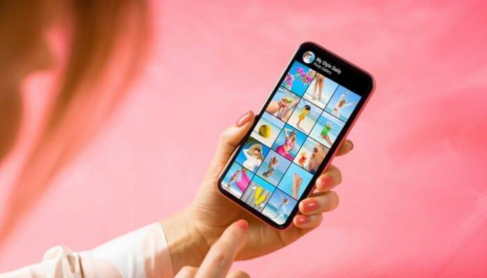 Na imagem, vemos um fundo rosa e uma pessoa segurando um celular com várias imagens na tela.