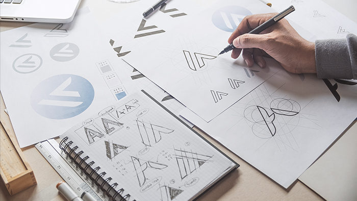 Saiba como a marca registrada protege seu negócio contra cópias não autorizadas Pessoa desenhando o logotipo de uma empresa para representar marca registrada.