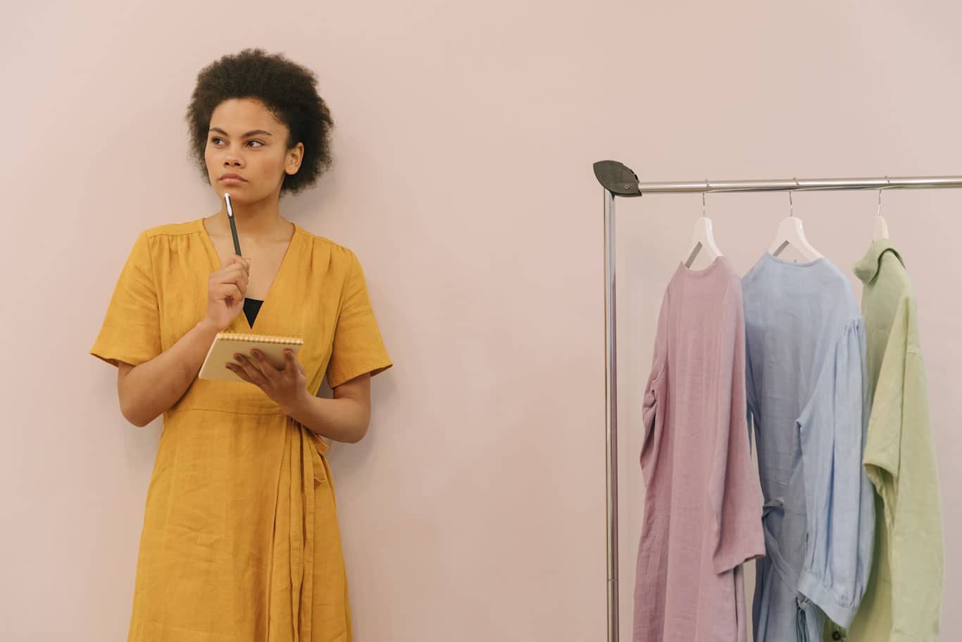 Mujer emprendedora pensando cuál es la diferencia entre persona física y moral junto a un rack de ropa