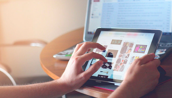 O que é figital e como adotar esse modelo de vendas? Close de mãos selecionando produtos de um e-commerce com estratégia figital em um tablet