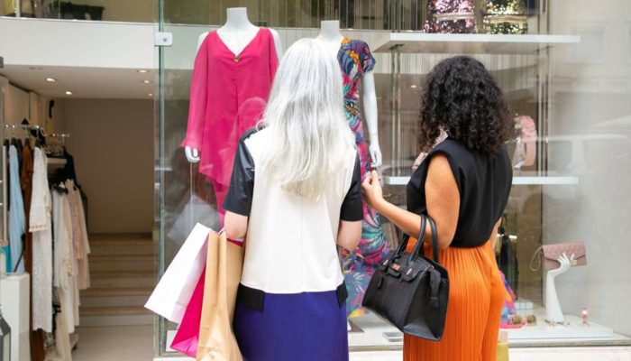 Para que serve e como aplicar o visual merchandising? Mulheres em frente a vitrine de loja de roupas observam o visual merchandising