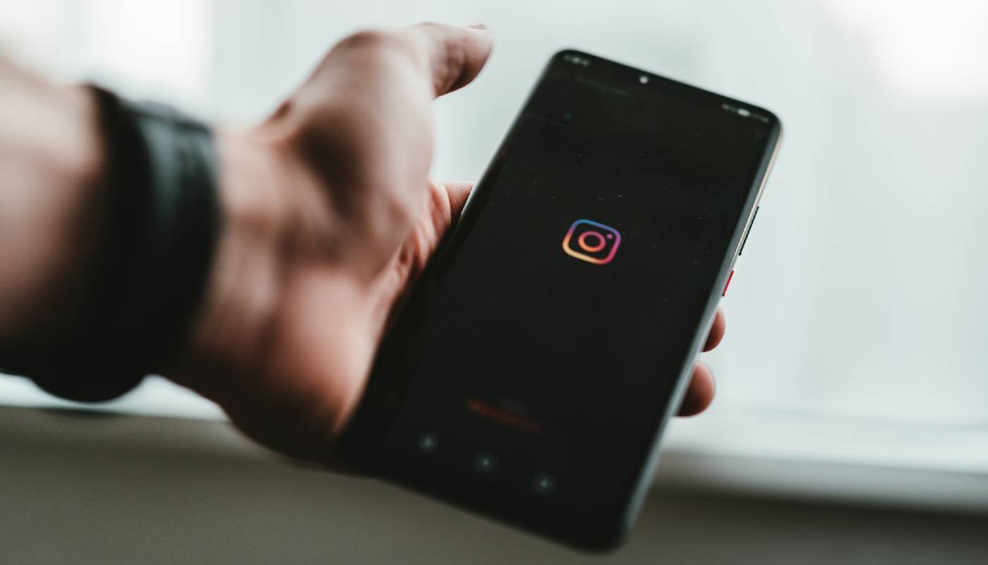 Mão segura celular com logo do Instagram na tela, representando como fazer promoção no Instagram