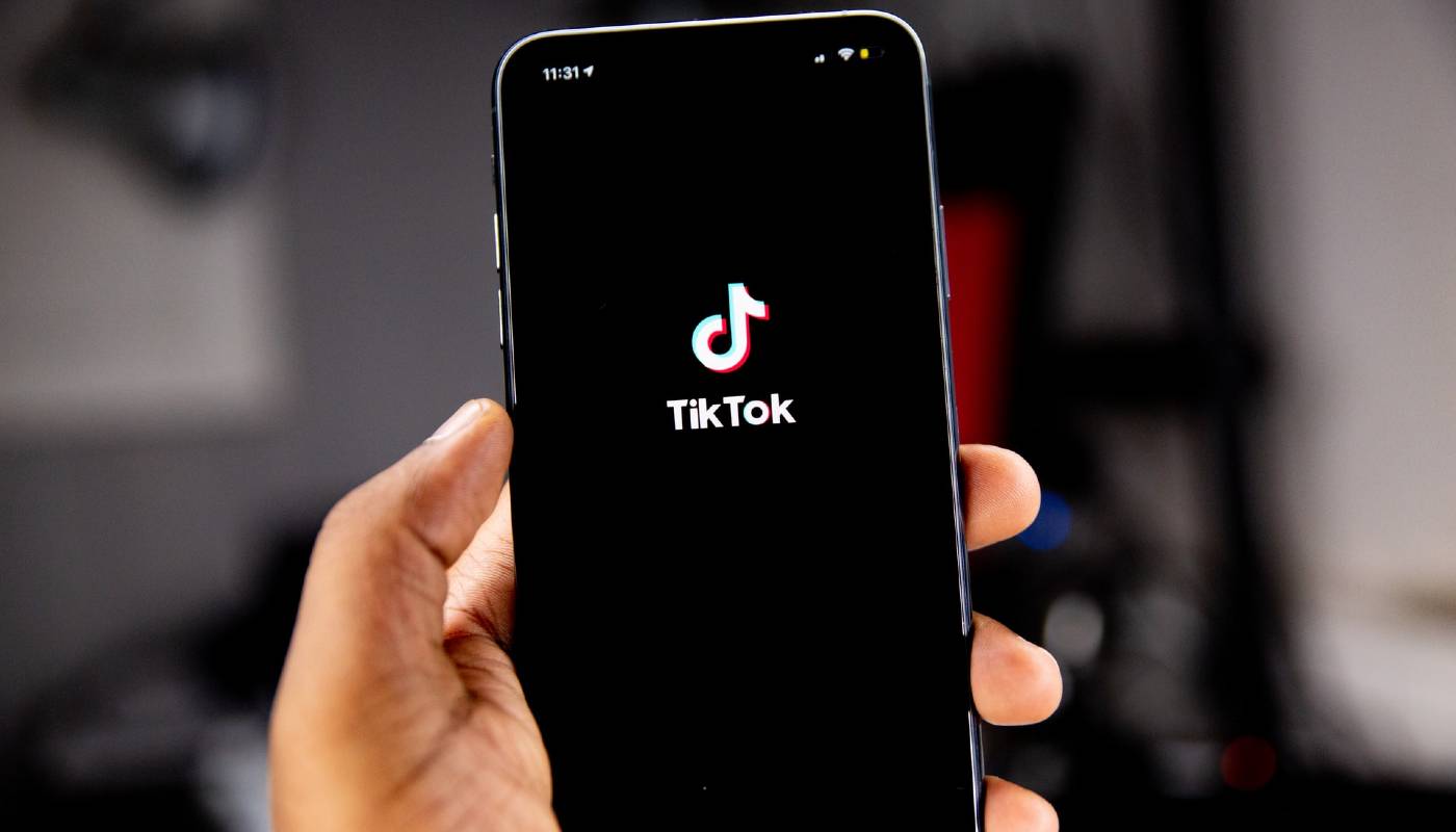 Pessoa segura celular com o logo da rede social, representando como usar o TikTok