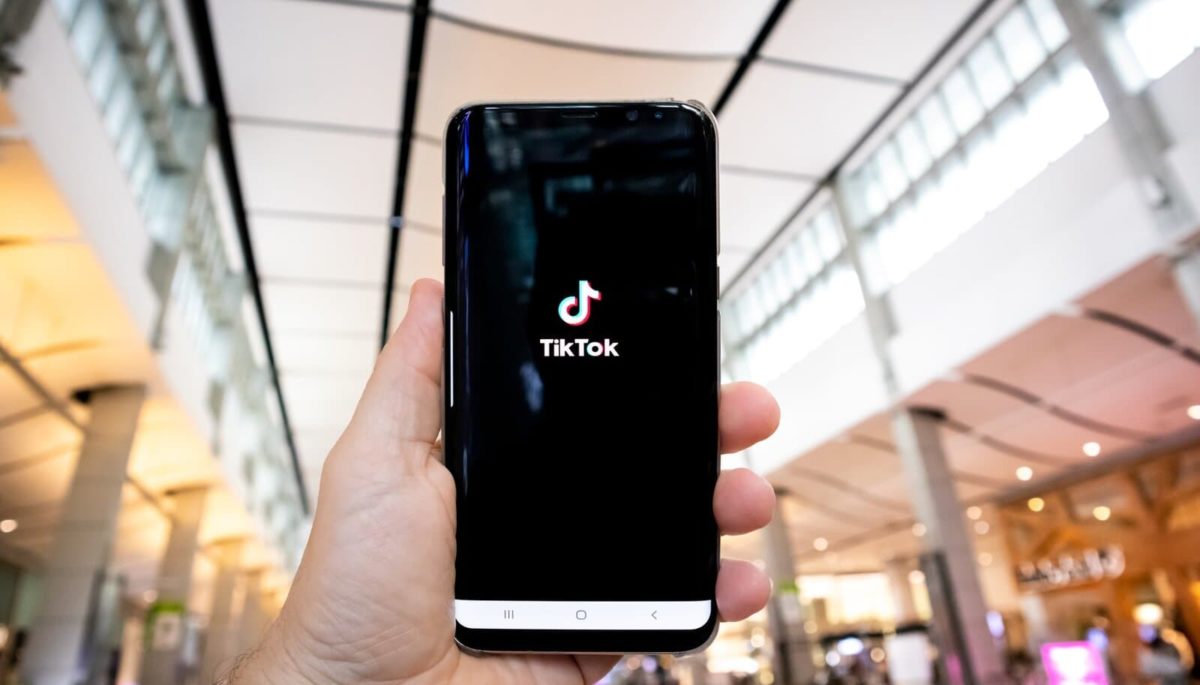 Imagem mostrando uma pessoa segurando o celular e abrindo o aplicativo do TikTok para seguir as dicas e ganhar seguidores no TikTok