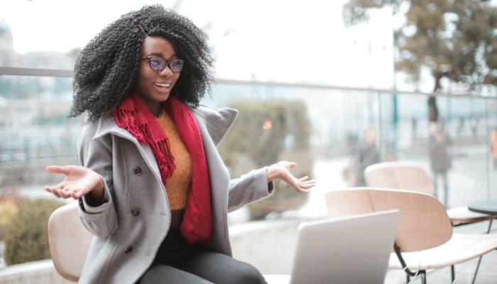 Mulher negra empolgada ao criar seu blog no Blogger em frente a um notebook