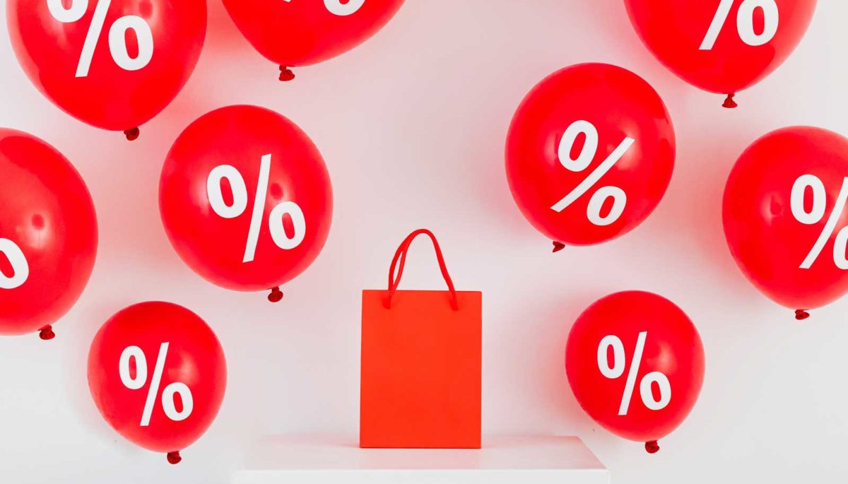 Sacola de compras e balões com o símbolo de porcentagem representam a estratégia de vendas downsell