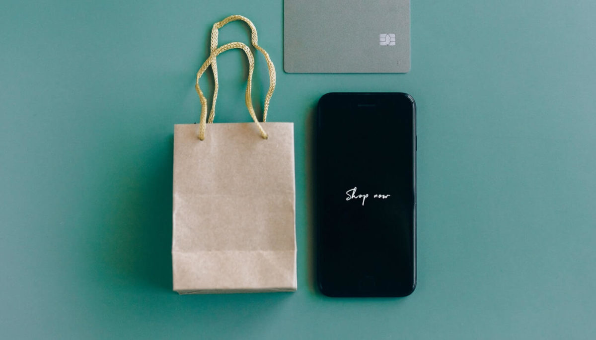 Imagem de sacola, smartphone e cartão de crédito sobre fundo colorido representa o que é loja virtual