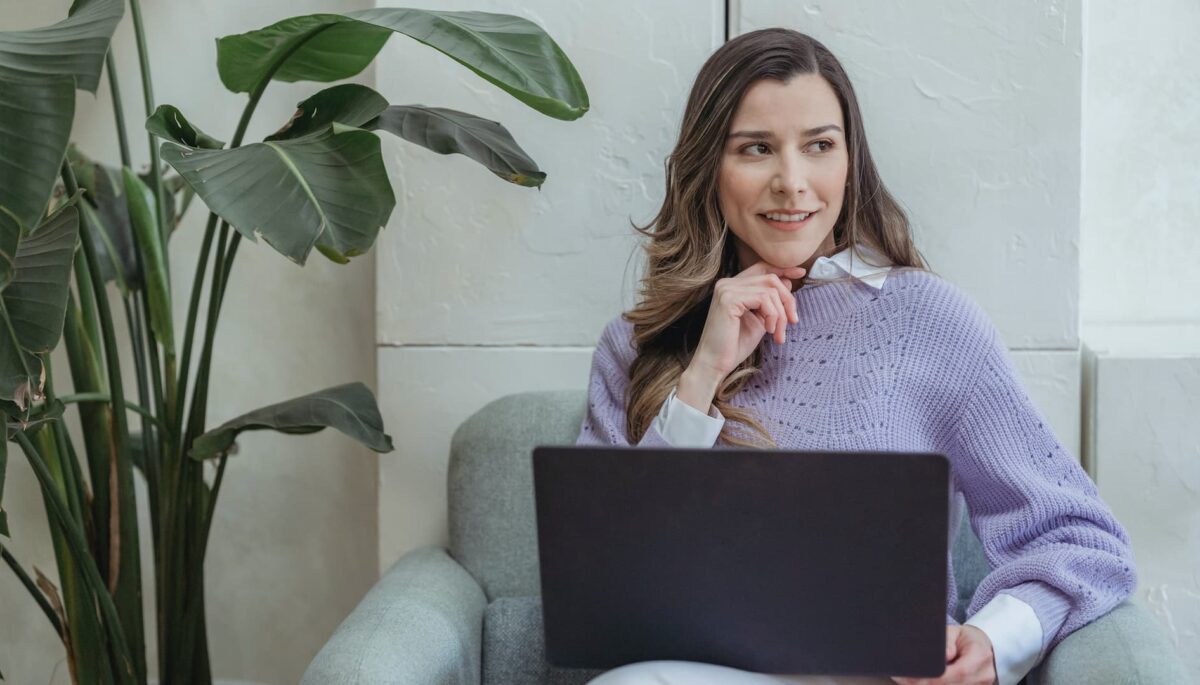 Mujer sentada en sillon con laptop en las piernas redactando los objetivos smart de su empresa