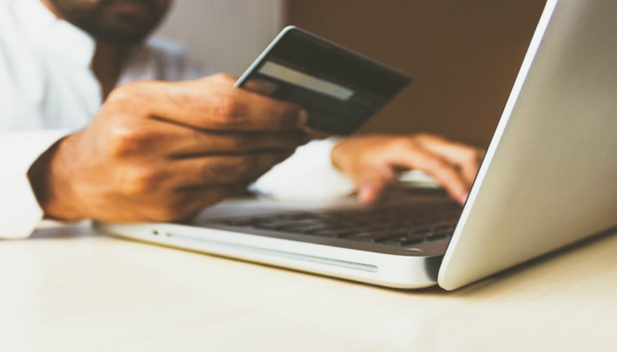 Usuário segura cartão de crédito enquanto digita no computador, representando a user experience ou experiência do usuário no e-commerce