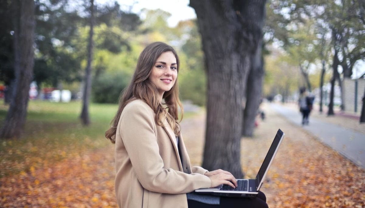 Mulher sentada em um banco de praça e trabalhando no notebook representando um freelancer de programação