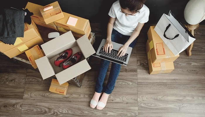 Foto de uma mulher sentada digitando no notebook e rodeada de caixas com produtos para representar a venda e integração com marketplace.