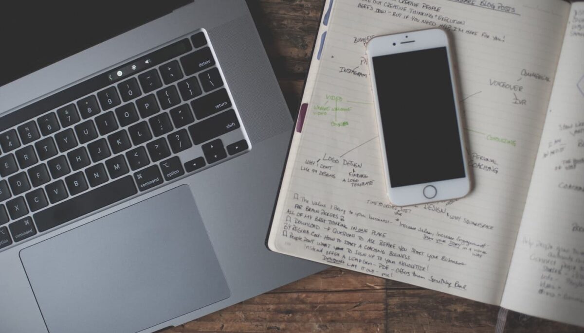 Notebook, caderno e smartphone sobre mesa representam a organização do plano de mídia
