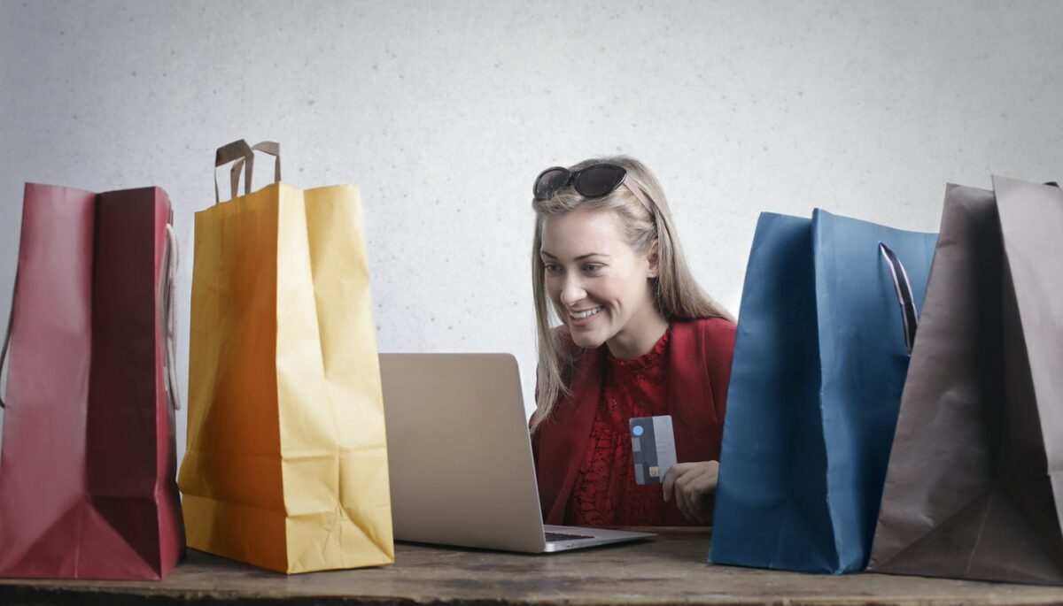 Mulher rodeada de sacolas e segurando cartão de crédito, como quem compra em um shopping virtual