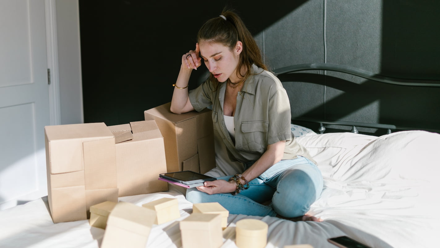 Emprendedora apasionada revisando sus pedidos en tablet sobre su cama llena de cajas 