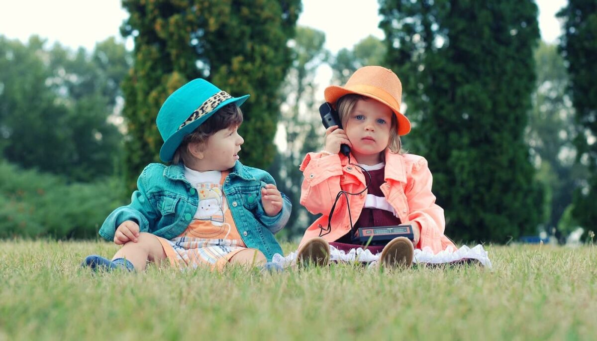 Duas crianças sentadas na grama, como se fossem modelos de alguém aprendendo como montar uma loja de roupas infantil