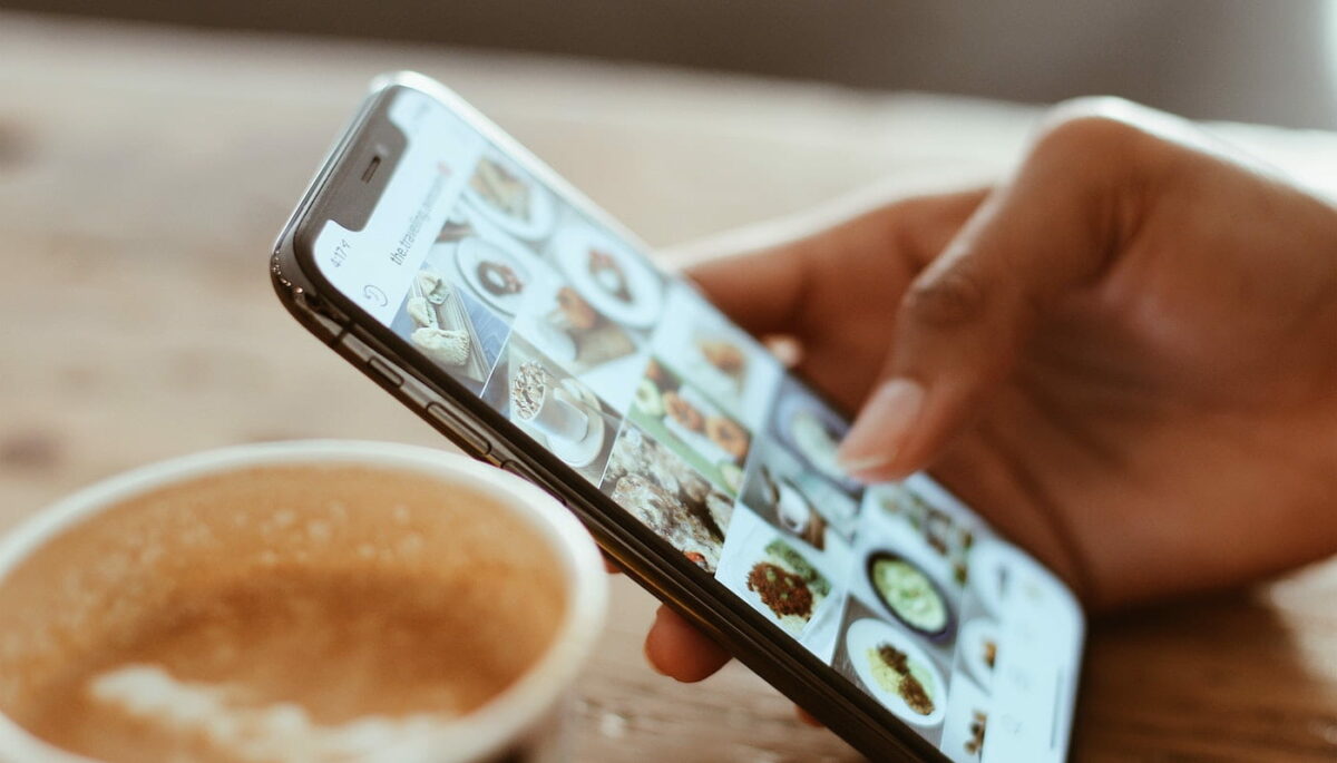 Mão segurando celular com o Instagram aberto, como quem está aprendendo como repostar no instagram