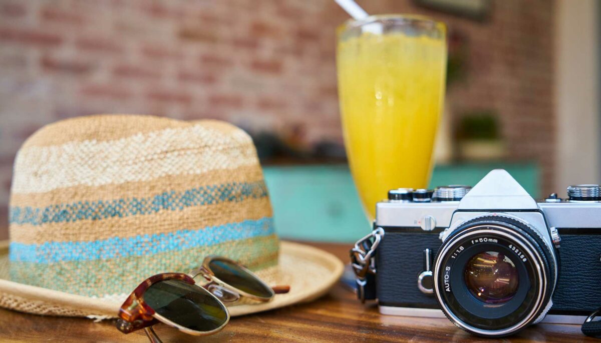 Mesa con cámara, lentes, un sombrero, un jugo en unas vacaciones de verano
