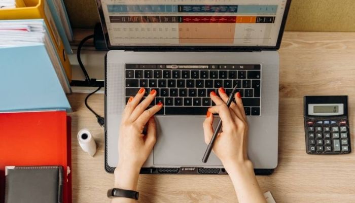 manos de mujer calculando los costos fijos y variables sobre una laptop